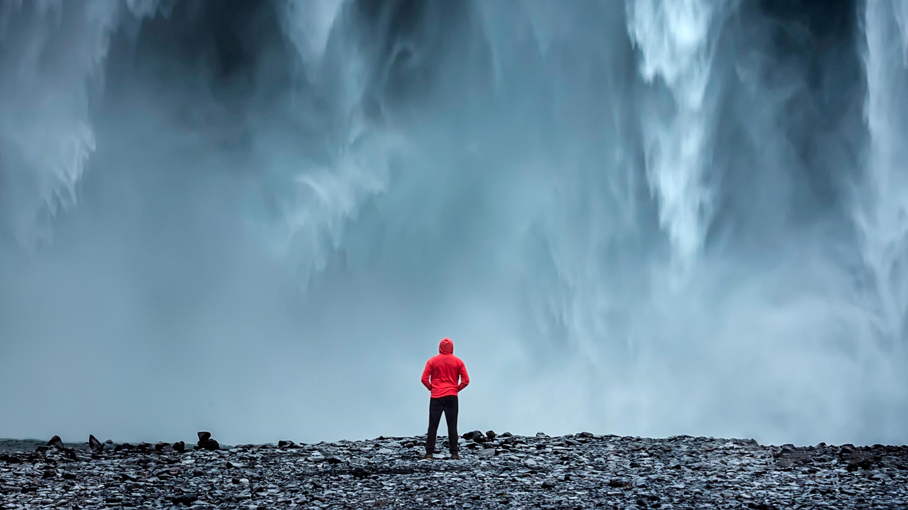 A man dressed in red in front of a waterfall